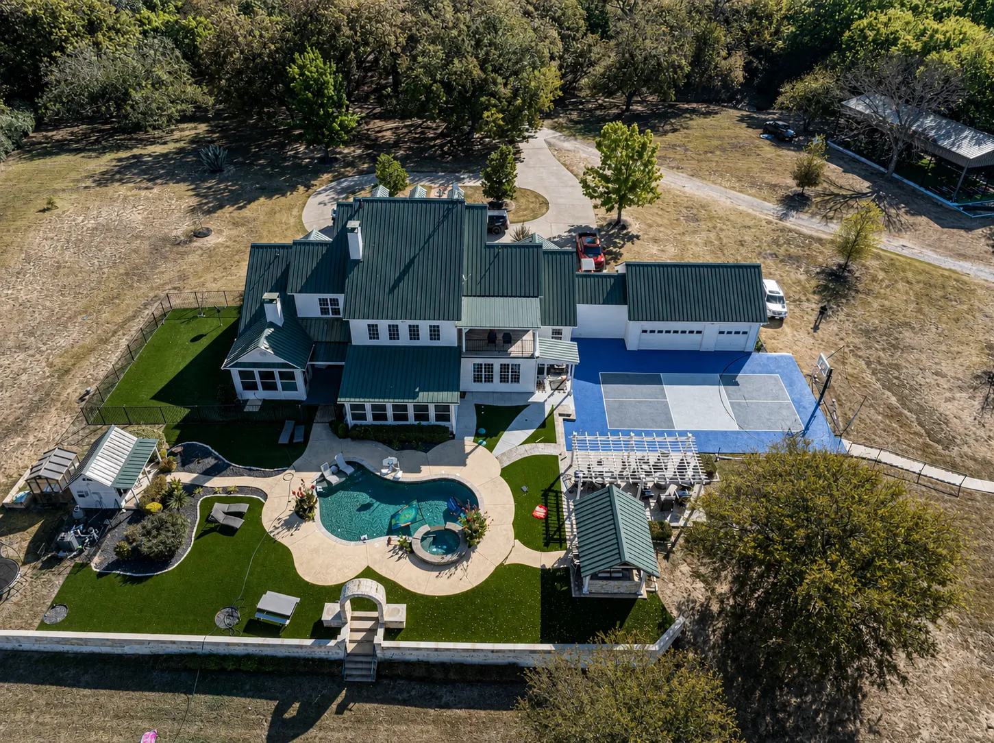Green-roofed estate with pool, pickleball court, turf, and pergola